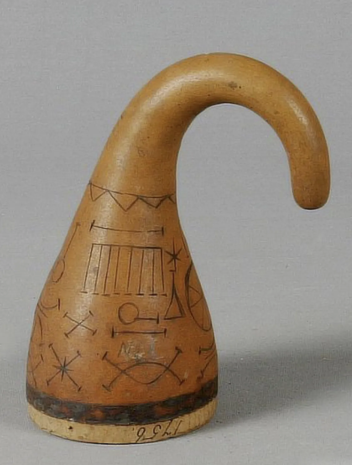 A hook-necked gourd on grey, incised with Nsibidi signs (crossed arcs, a comb shape, a star and a circle on a line), with a dark band at the base and a number inked on it.