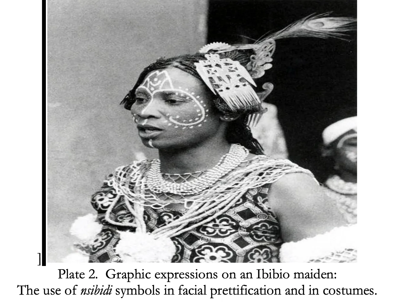 A black-and-white photograph of a young woman with white dotted designs painted on her face, a carved comb in her hair and many strands of beads, captioned “Graphic expressions on an Ibibio maiden: the use of nsibidi symbols in facial prettification and in costumes.”
