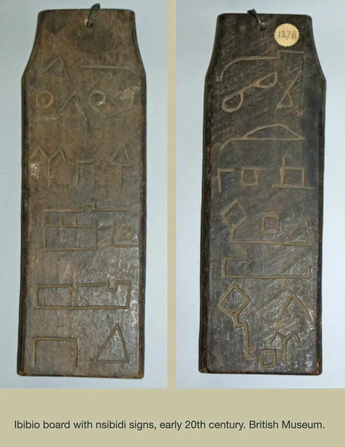 Both faces of a dark wooden board with a metal hanging loop, carved with Nsibidi signs: triangles, circles, house-like outlines and forked signs; a paper label reads 1278. The caption reads “Ibibio board with nsibidi signs, early 20th century. British Museum.”